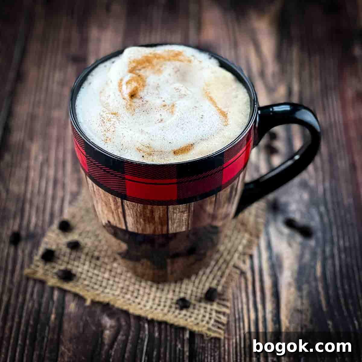 A large mug filled with a delicious homemade latte, topped with a sprinkle of cinnamon, with loose coffee beans on the table.