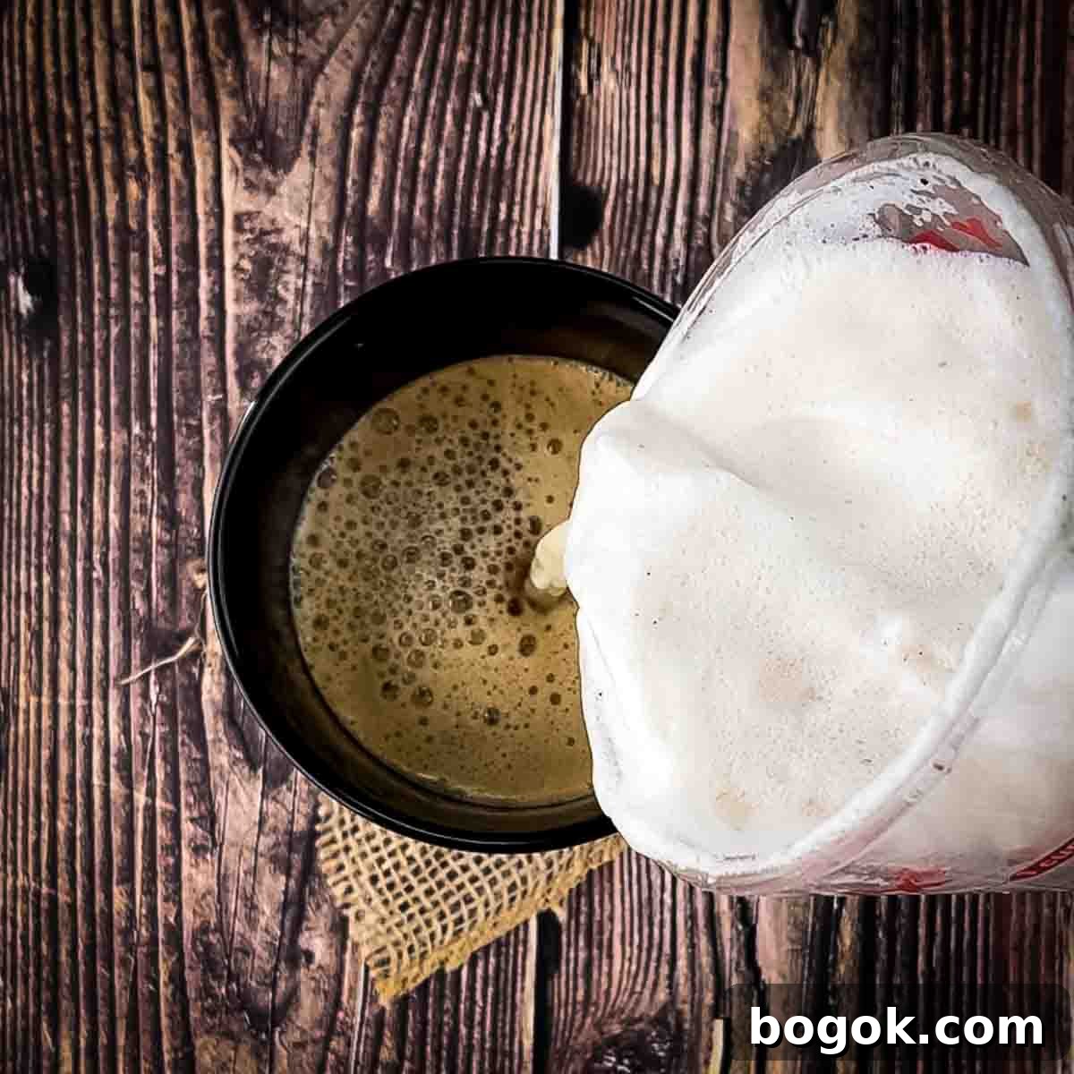 The steamed milk being poured on top of the espresso in a black mug.
