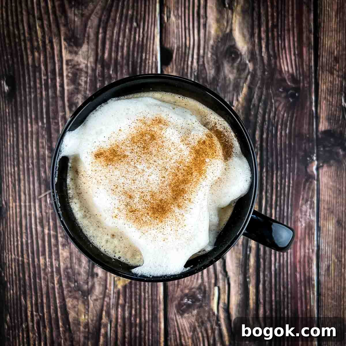 Cinnamon sprinkled on top of the latte in a black mug.