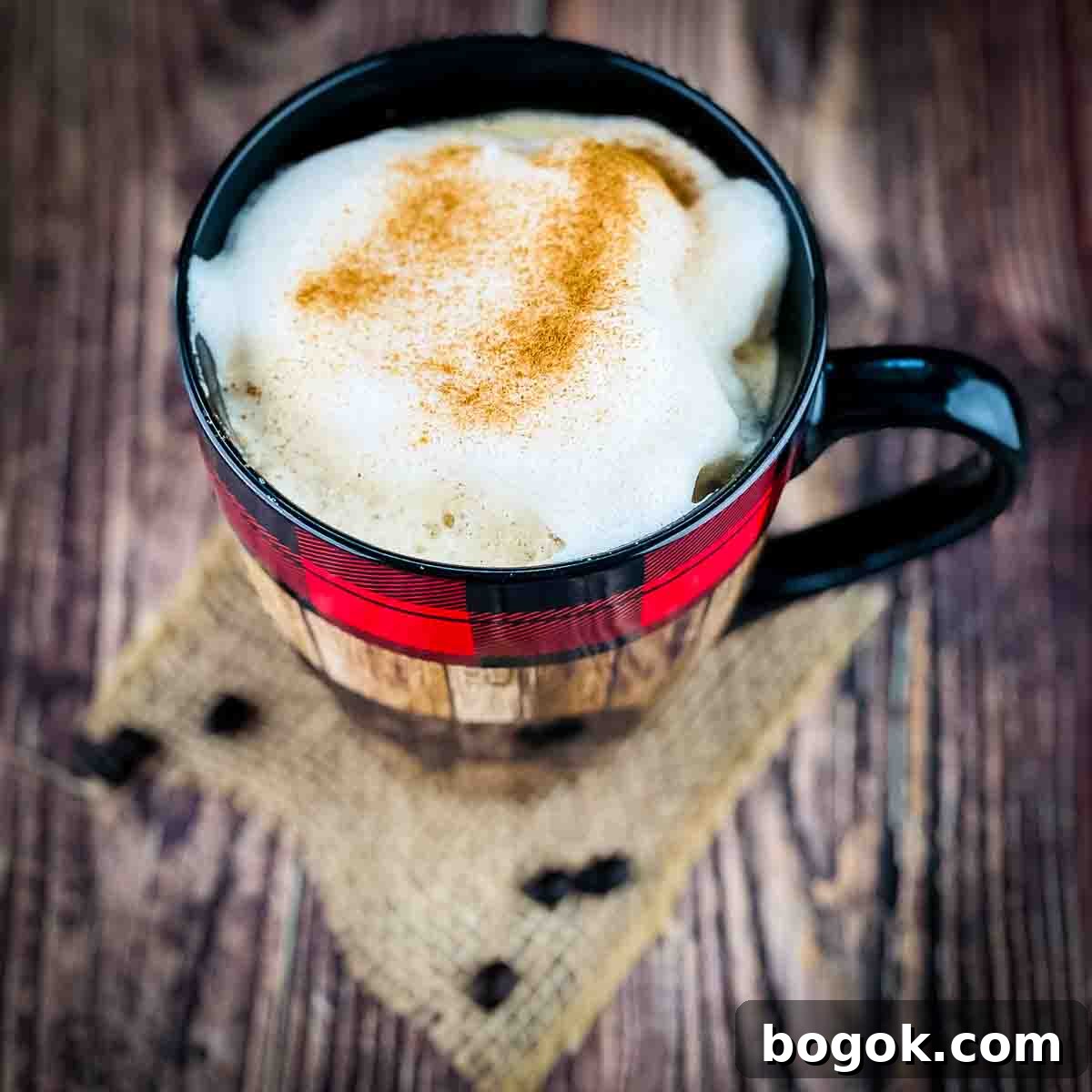 A large mug filled with a delicious homemade latte, topped with a sprinkle of cinnamon, with loose coffee beans on the table.