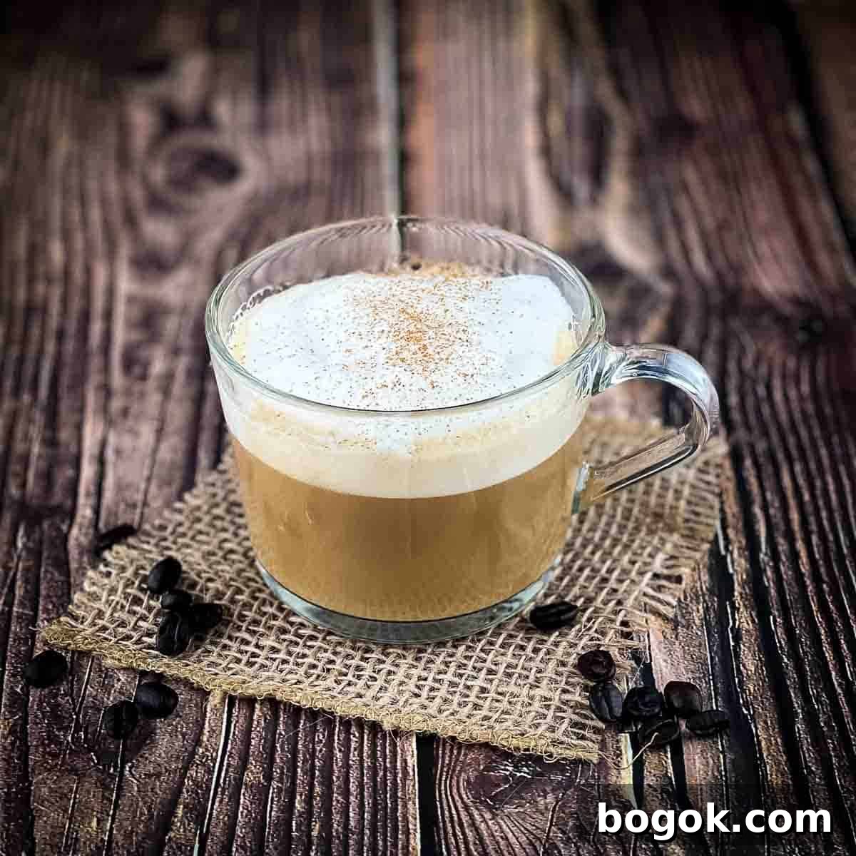 A large mug filled with a delicious homemade latte, topped with a sprinkle of cinnamon, with loose coffee beans on the table.