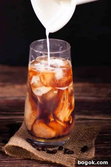 Cream being poured over coffee and ice cubes in a tall glass to make the perfect iced coffee at home.
