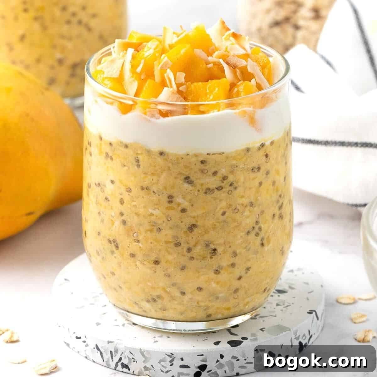 Glass jar of mango overnight oats, topping with yoghurt, mango pieces and some flaked coconut.