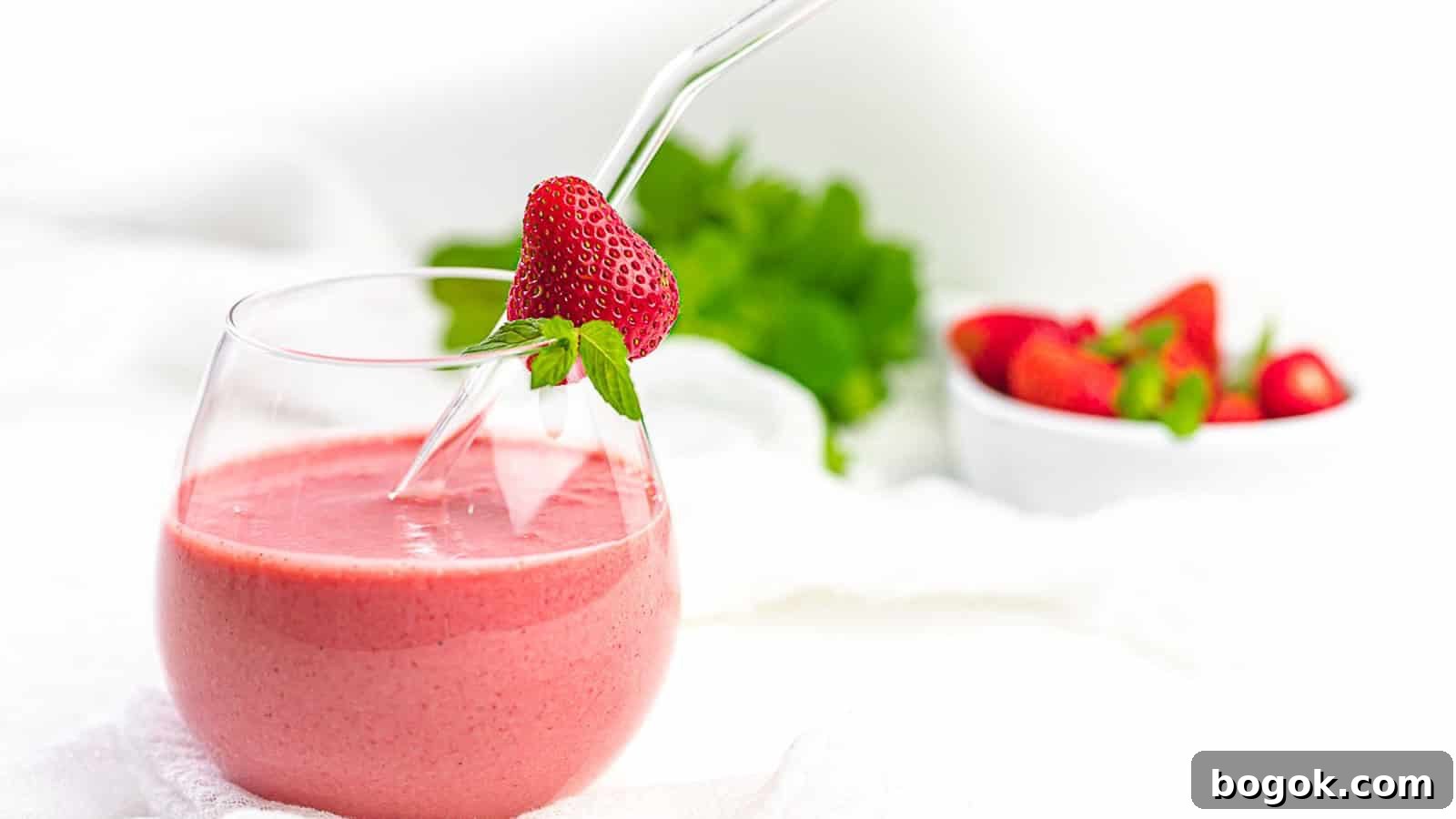 Strawberry Mint Keto Smoothie inside a glass with straw and fresh strawberry.