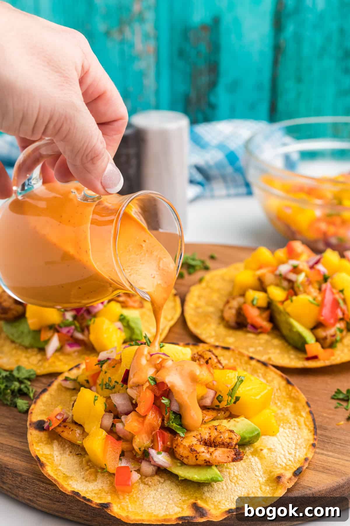Mango Salsa Grilled Shrimp Tostadas with Chipotle Cream 4 Sauce is being drizzled over a tostada.