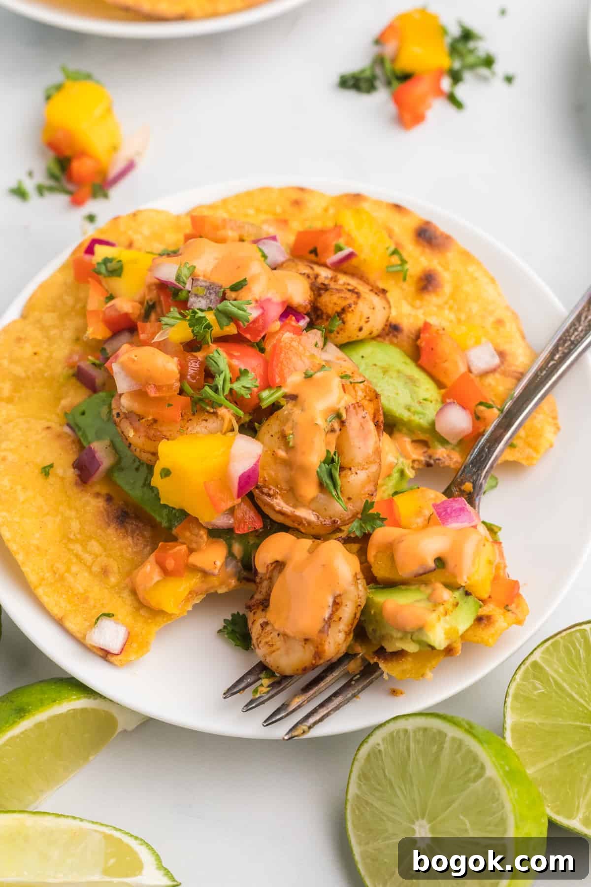Mango Salsa Grilled Shrimp Tostadas with Chipotle Cream 5 A fork is placed on a white plate with a shrimp tostada.