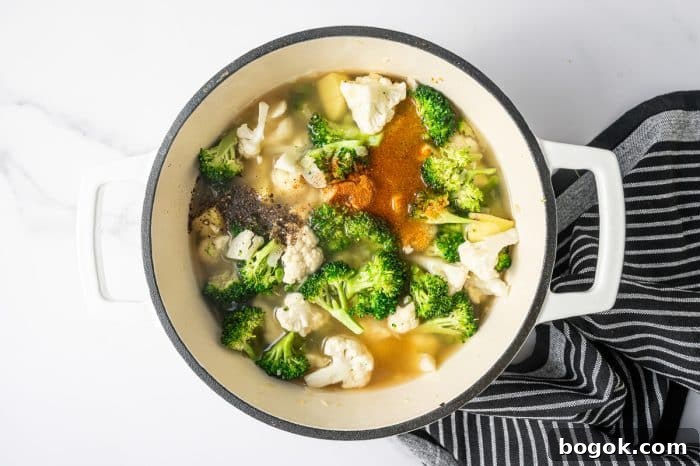 Creamy Broccoli and Cauliflower Soup Recipe for Comforting Meals 5 Overhead shot of a cream enameled Dutch oven filled with broth covering broccoli, cauliflower, and potato pieces.