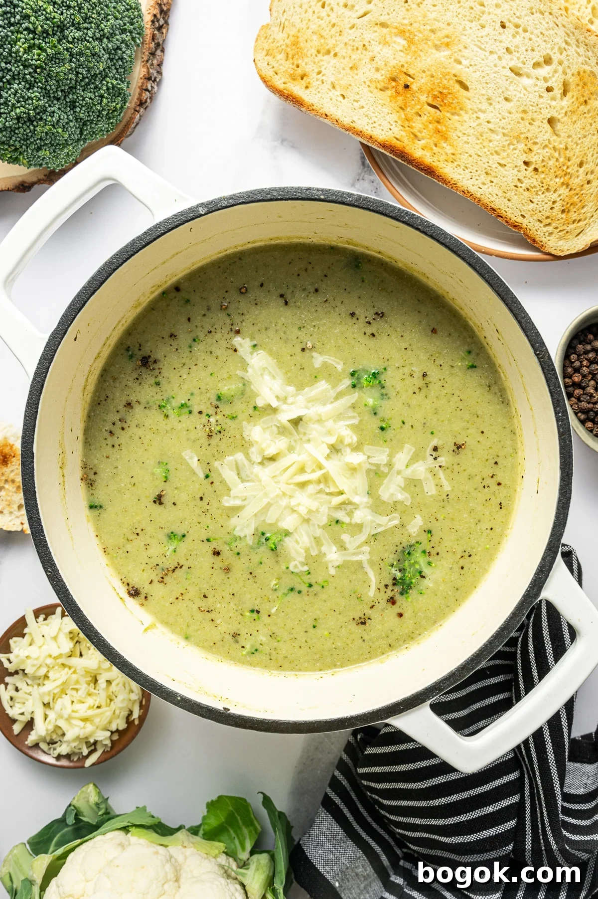 Creamy Broccoli and Cauliflower Soup Recipe for Comforting Meals 6 Overhead hero photo of broccoli cauliflower soup in a cream enameled Dutch oven. The soup is creamy pale green and topped with shredded cheddar, scattered black pepper, and a few small broccoli florets.
