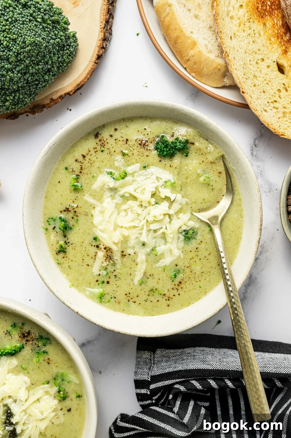 Creamy Broccoli and Cauliflower Soup Recipe for Comforting Meals 7 Overhead serving photo of broccoli cauliflower soup in a light beige bowl. The soup is topped with shredded cheddar, cracked black pepper, and a few broccoli bits, with a gold-handled spoon resting in the bowl.