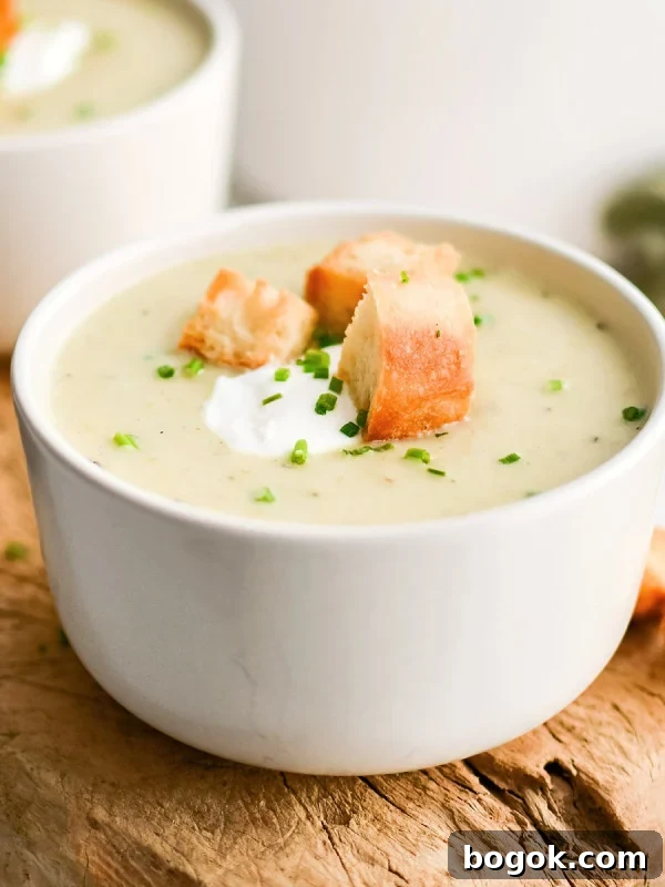 Creamy Broccoli and Cauliflower Soup Recipe for Comforting Meals 8 White soup bowl on a rustic wood board filled with homemade creamy potato leek soup and garnished with sour cream, homemade croutons, and freshly chopped chives.