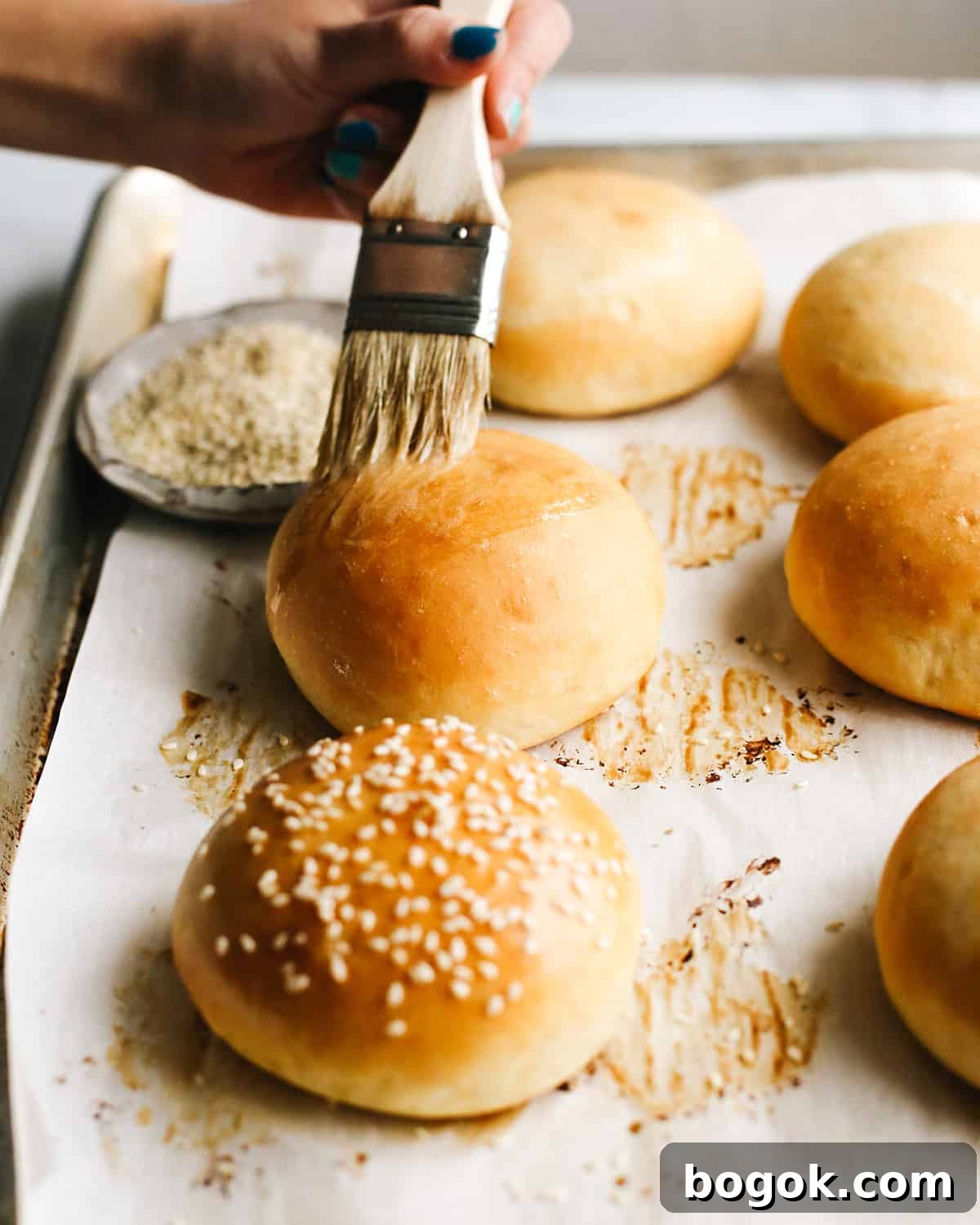 butter being brushed onto the top of a homemade hamburger bun
