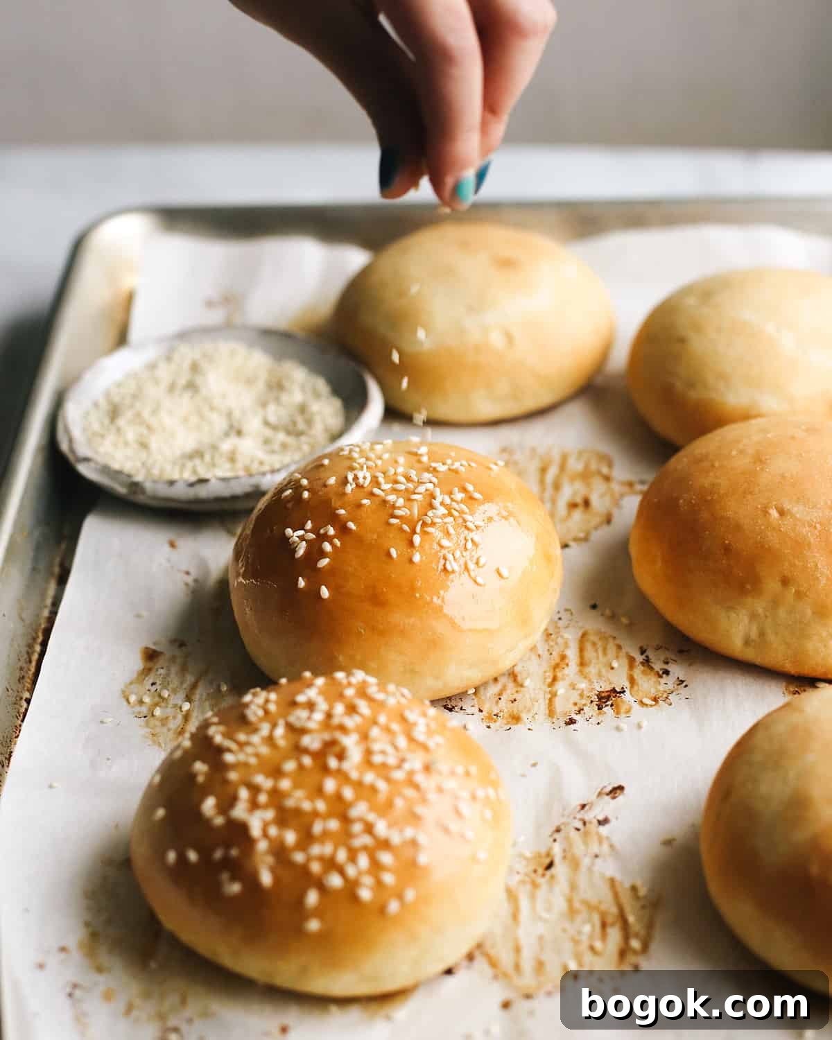 front view of sesame seeds being sprinkled on Homemade Burger Buns