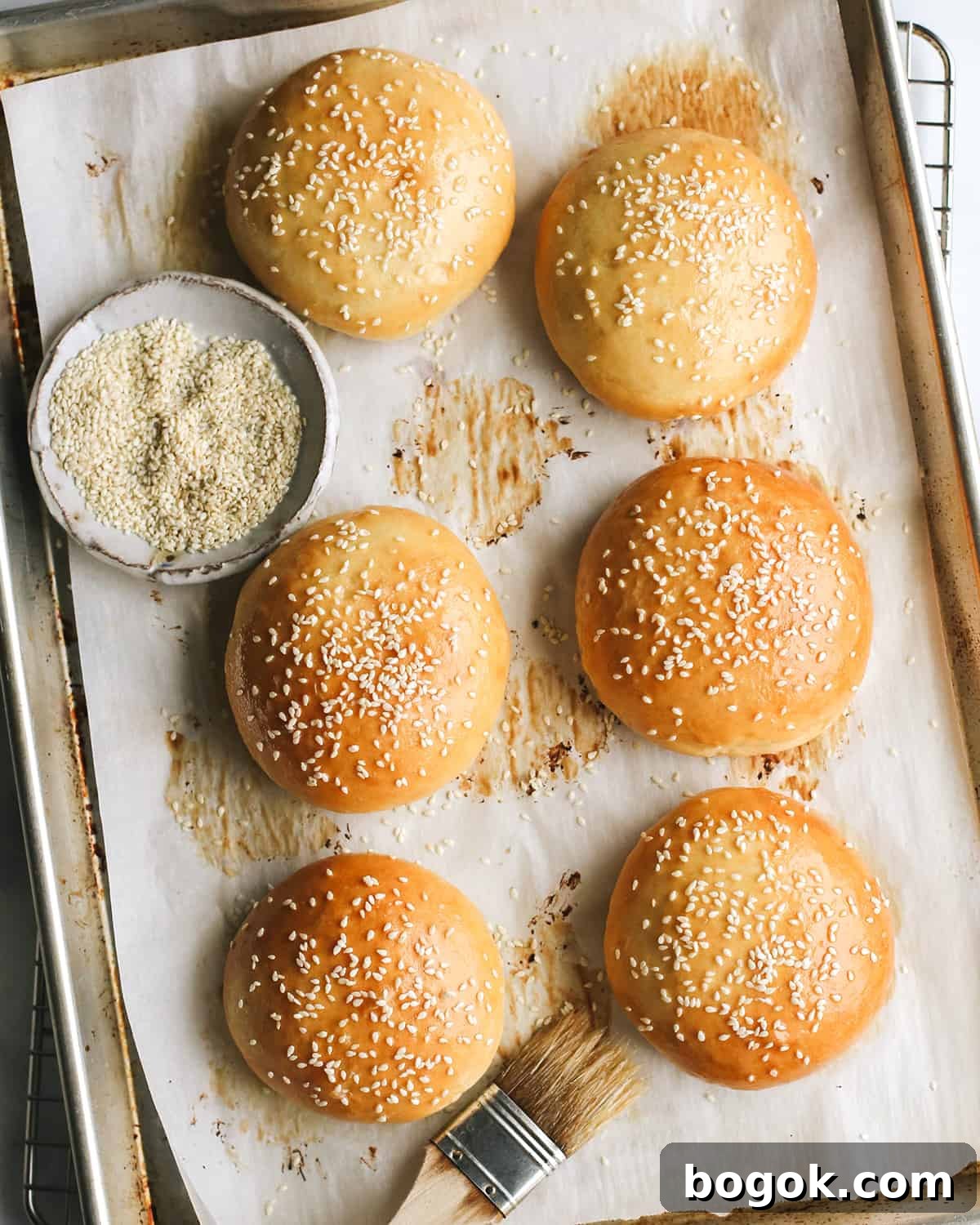 6 Homemade Hamburger Buns on a baking sheet after baking topped with sesame seeds 