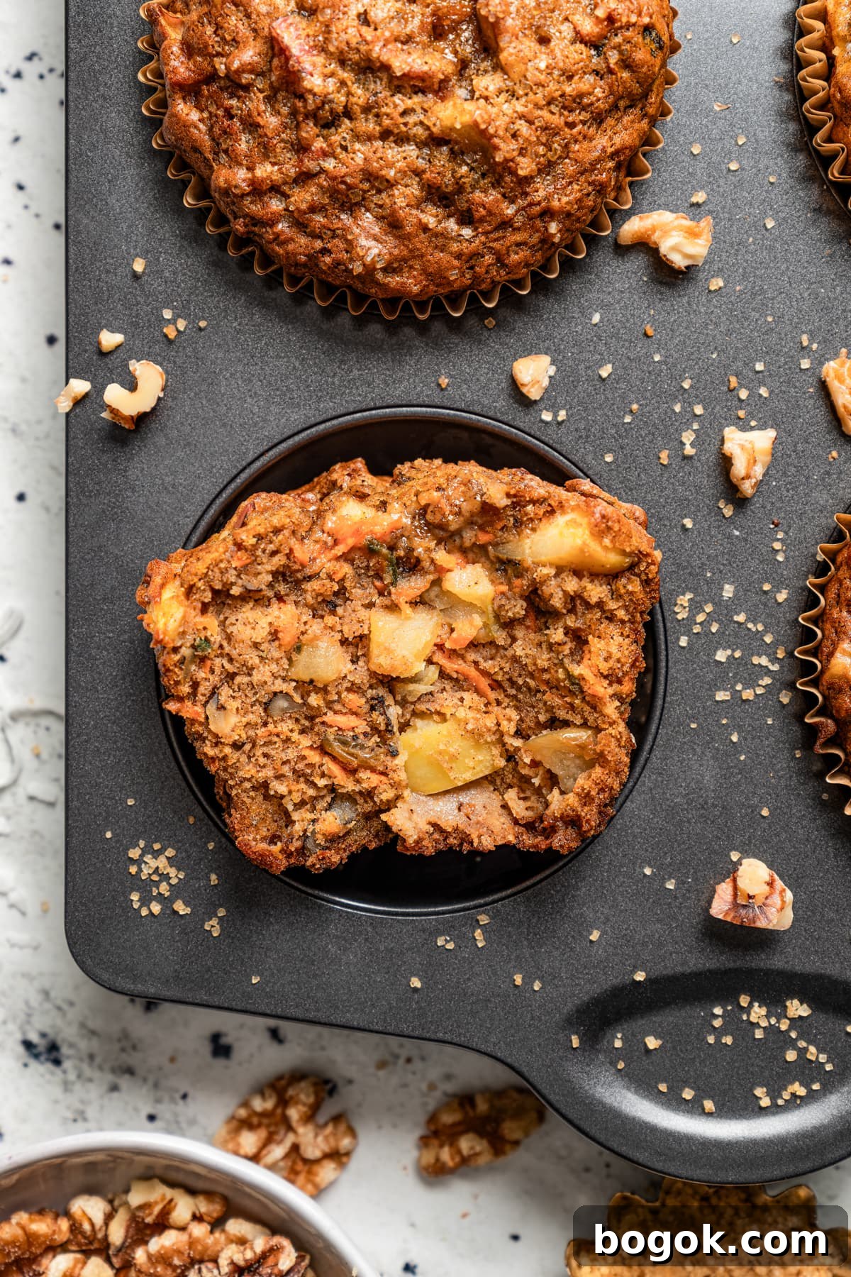 This jumbo morning glory muffins recipe with fruity and nutty add-ins is packed with warm spices for the perfect breakfast bite. Halved morning glory muffin in a pan.
