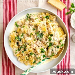 In a white bowl, Crockpot Creamy Chicken Pasta is topped with parsley and grated cheese.