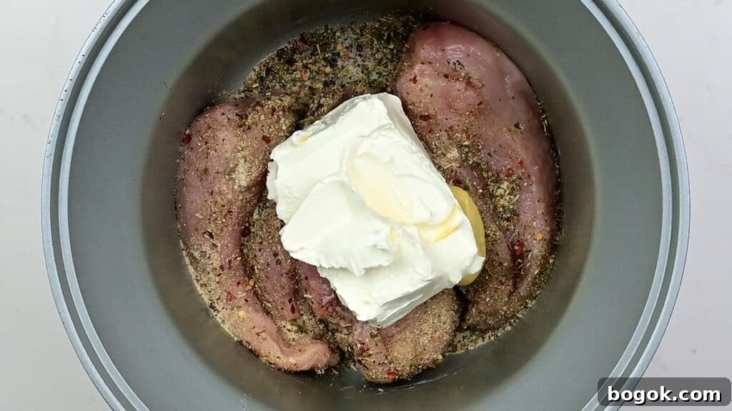 seasoned chicken breasts topped with cream cheese in a slow cooker