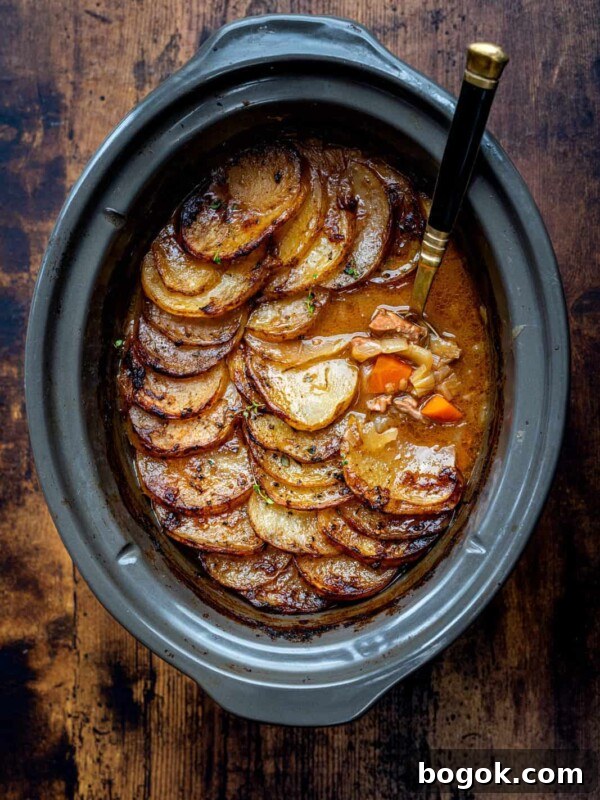A slow cooker filled with golden, thinly sliced potatoes layered over a hearty lamb stew