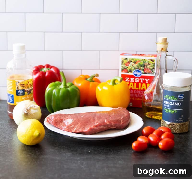 Steak, peppers, onion, lemon, Italian mix, olive oil, oregano and cherry tomatoes on a granite counter.