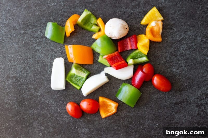 Chopped red, green, and yellow peppers with tomatoes, mushrooms and onions on a granite counter.