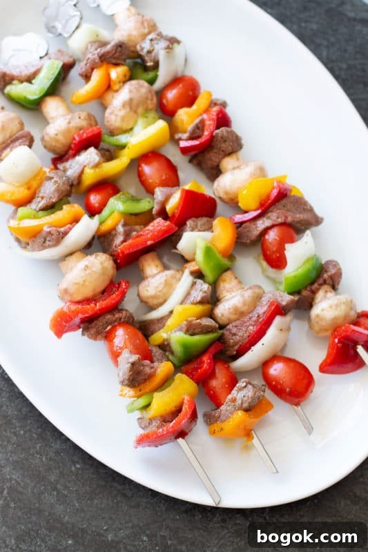 White platter containing four steak and vegetable skewers.