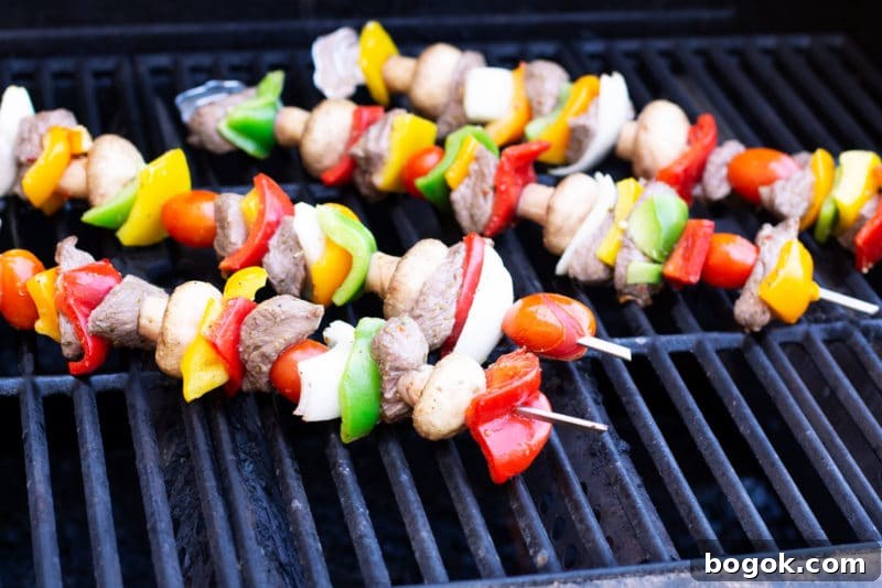 Four steak and vegetable skewers on the grill.
