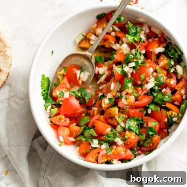 tomato, onion and coriander chopped salad in a white bowl on a light background. Spoon in the salad.