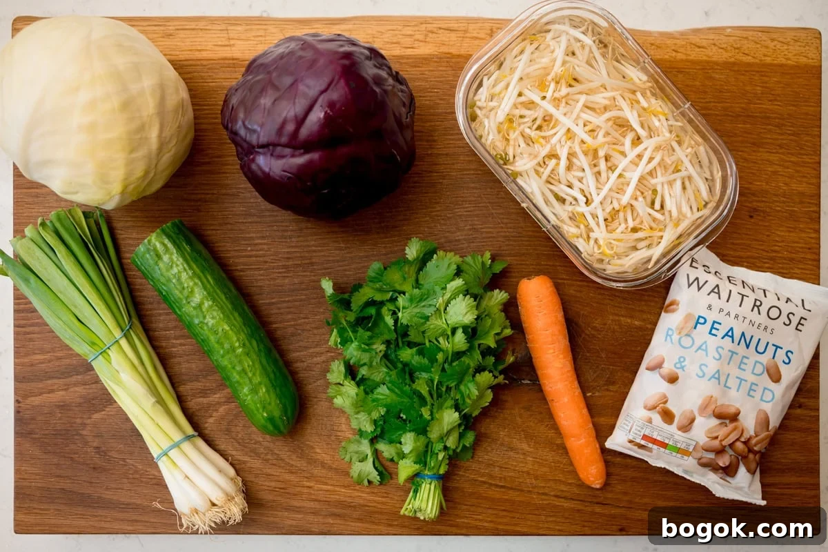 An overhead shot of the ingredients for Asian Slaw. They are laid out on a wooden cutting board. They are red and white cabbage, Spring onions, Cucumber, Coriander, a carrot, Beansprouts and Roasted and Salted Peanuts.