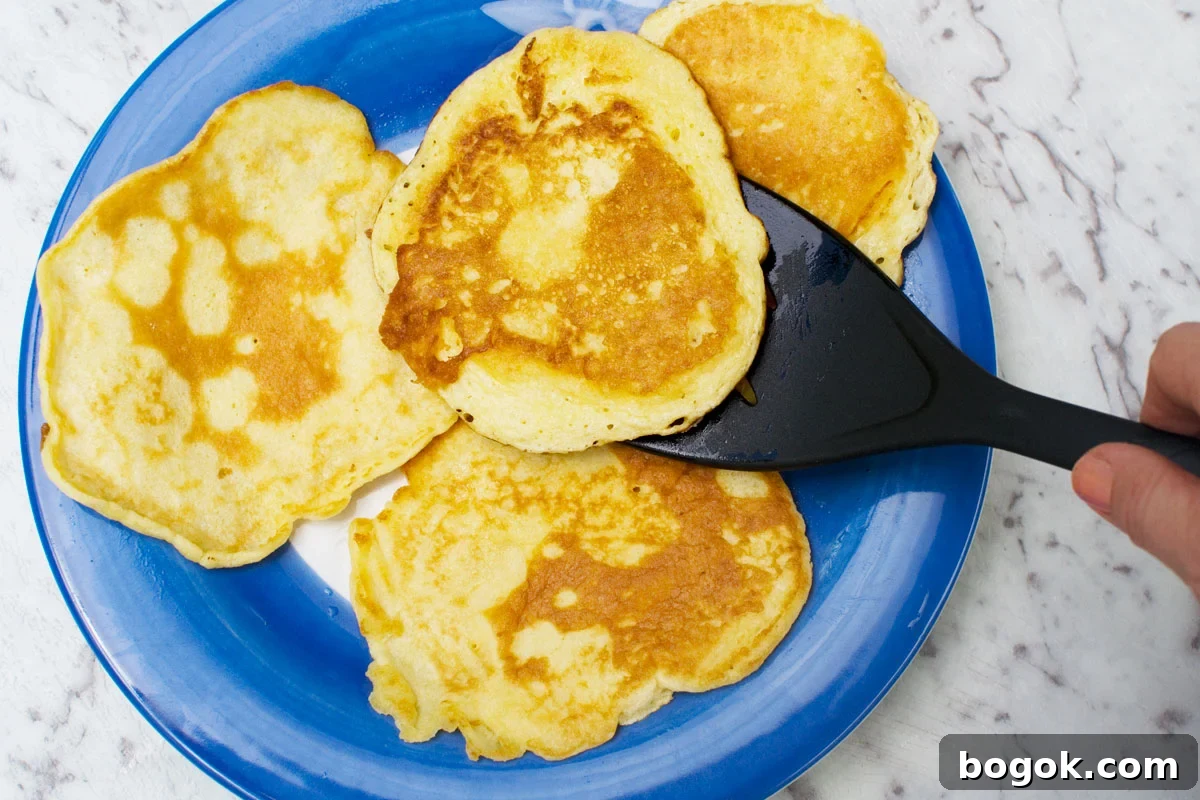 Fluffy Pancakes with Caramelized Bananas and Maple Topping 5 4 pancakes on a blue plate - someone is lifting one off the plate with a black spatula