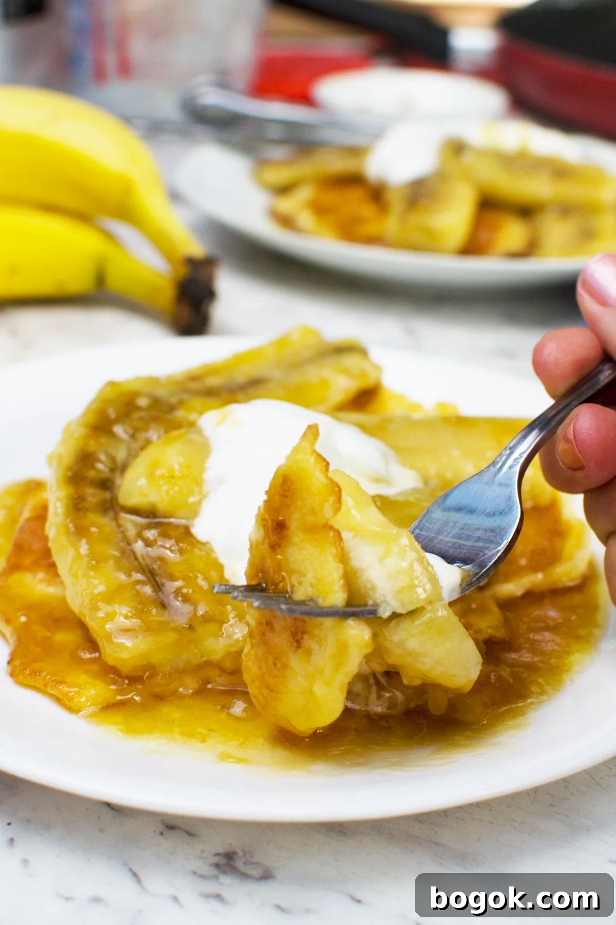 Fluffy Pancakes with Caramelized Bananas and Maple Topping 7 Someone eating a plate of caramelised banana pancakes - there are bananas and another plate of pancakes in the background