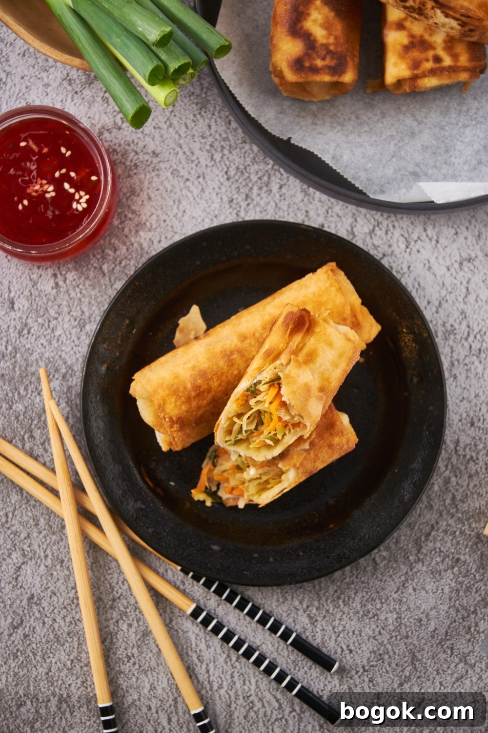 Overhead view of two fried egg rolls with one sliced in half and stacked on top of each other.