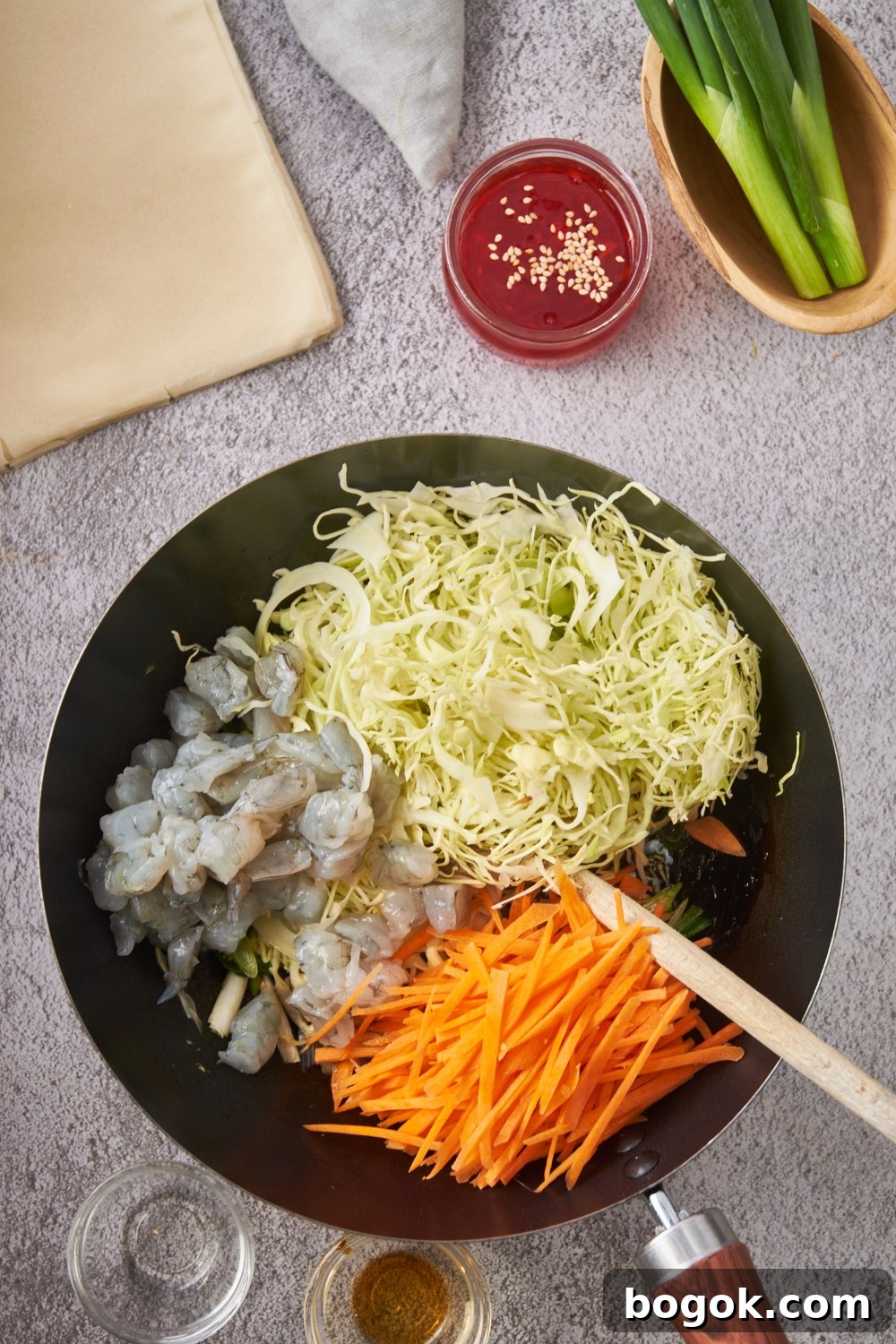 Skillet with raw shrimp, shredded cabbage, and shredded carrots.