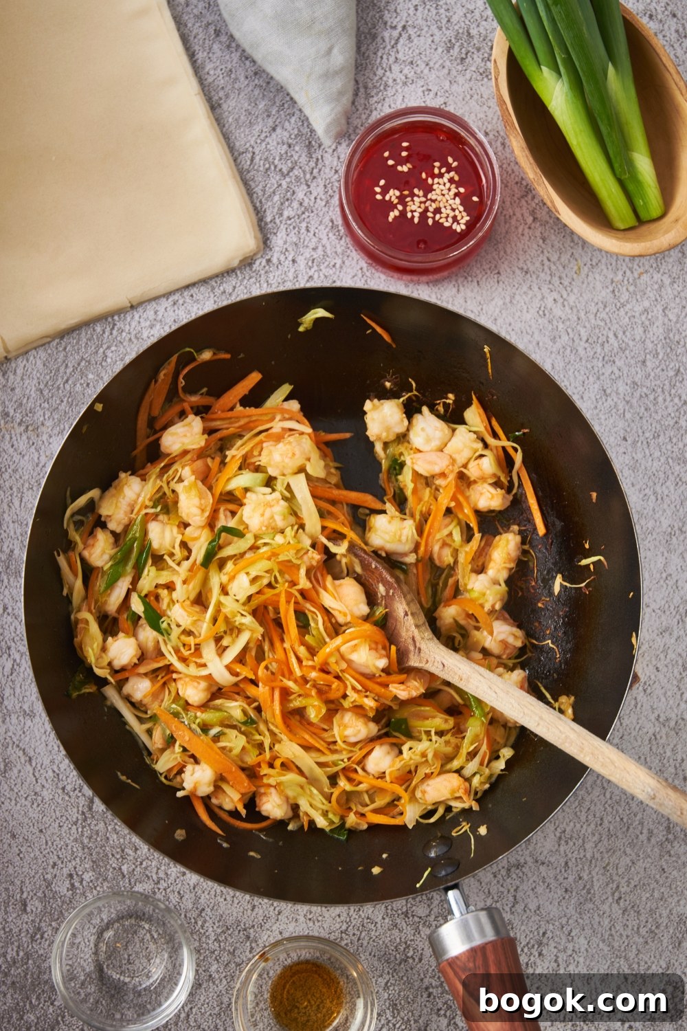 Skillet with diced shrimp, shredded carrots, cabbage, and green onions.