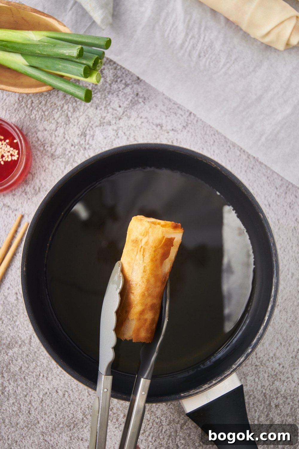 A fried egg roll being removed from a pot of oil using a pair of tongs.