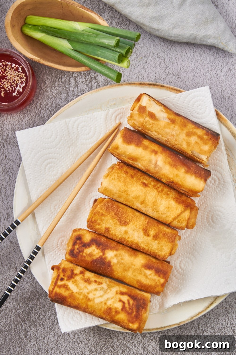 Six fried egg rolls lined next to each other on a plate lined with paper towels.