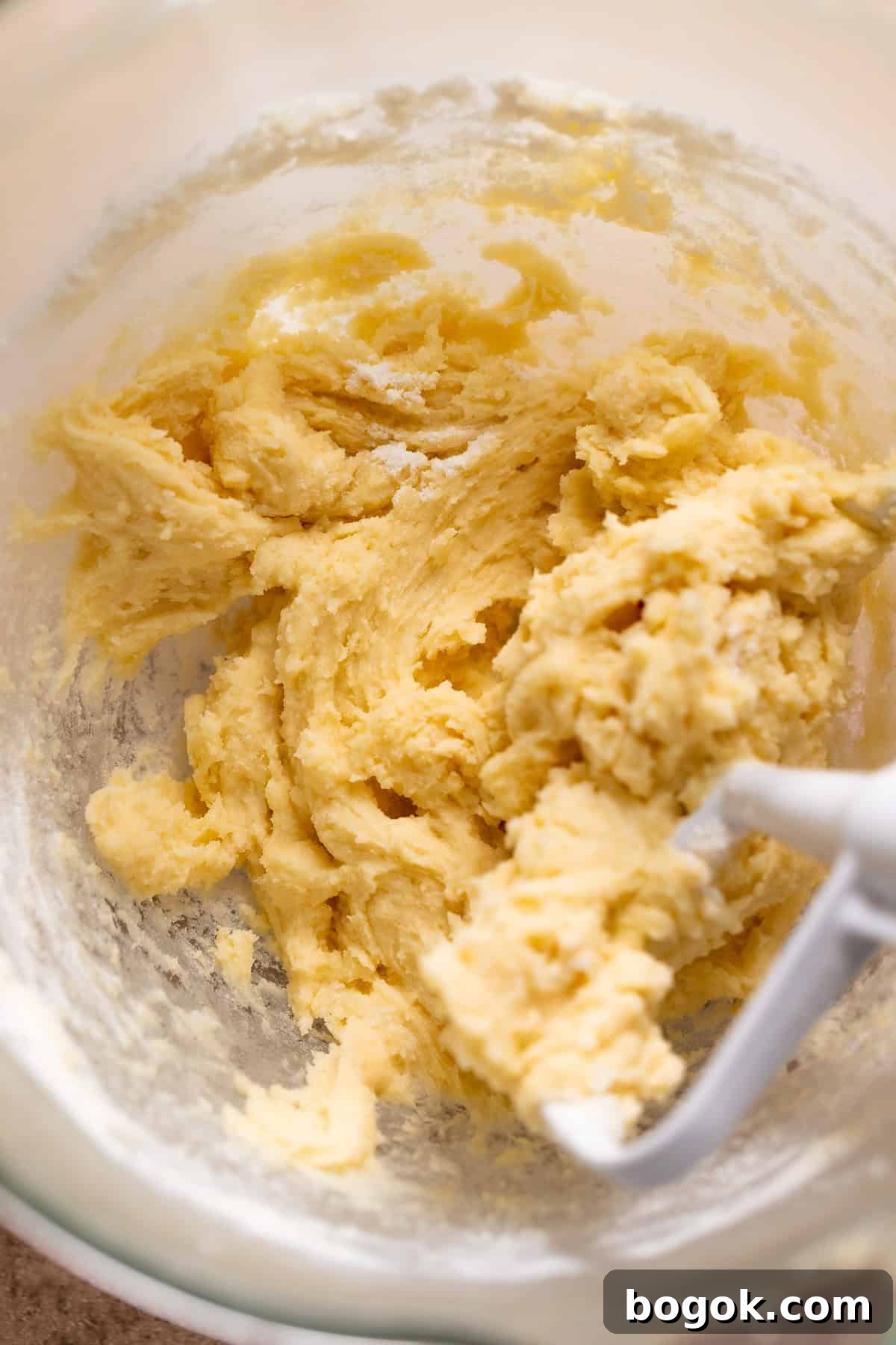 Sugar cookie dough filling in a glass mixer bowl with the paddle attachment.