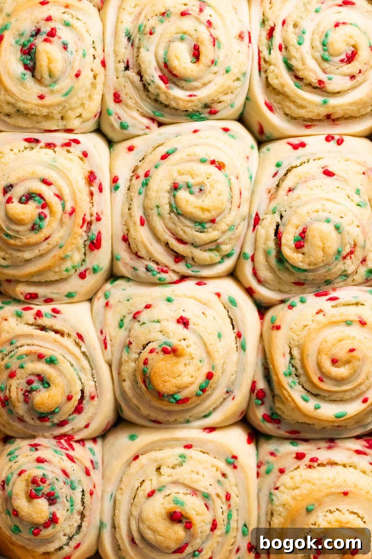 Baked sugar cookie rolls in a pan with visible red and green sprinkles before icing.