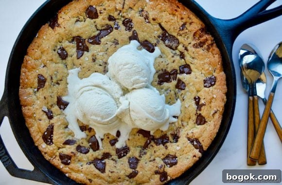 Homemade Skillet Chocolate Chip Cookie topped with three scoops of vanilla ice cream next to spoons