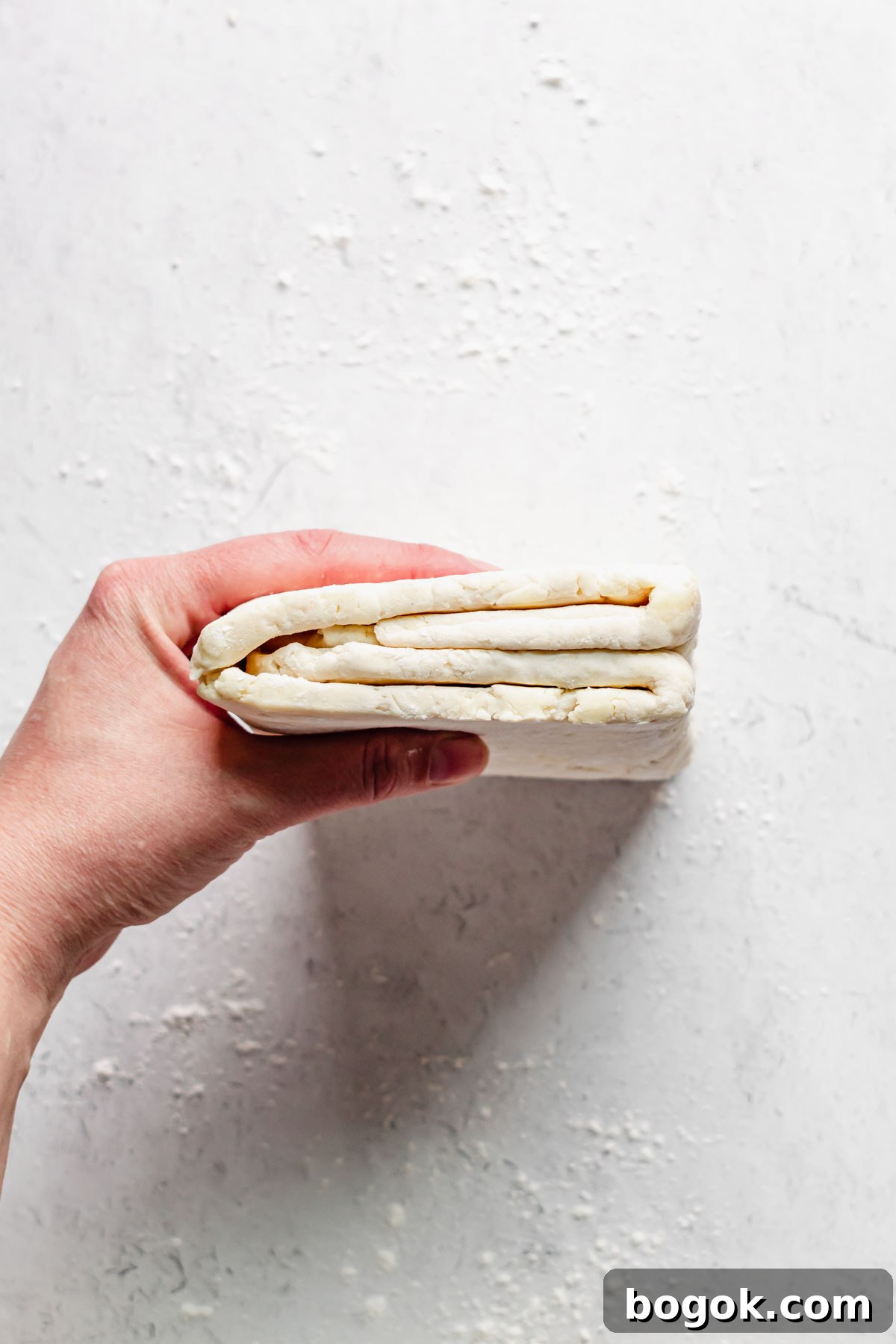A hand holds the dough up to show the trifold inside.