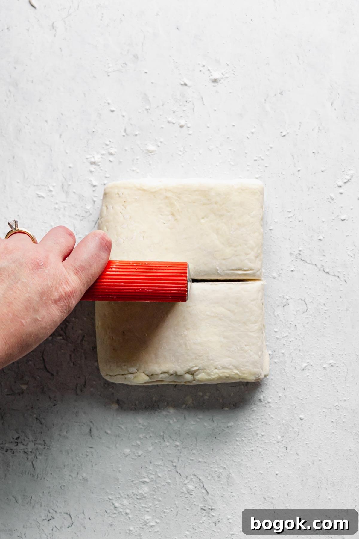 A bench scraper cuts the dough in half to make two sheets of rough puff pastry.