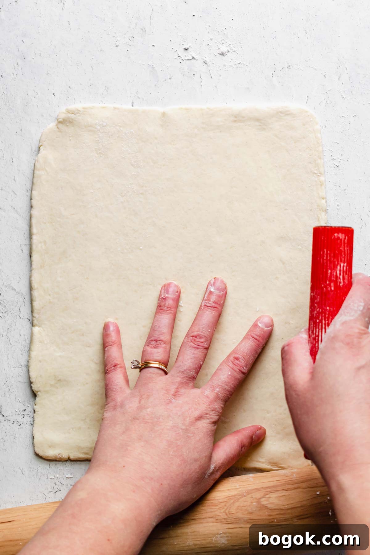 One half of the pastry rolled out with a bench scraper shaping the sides.