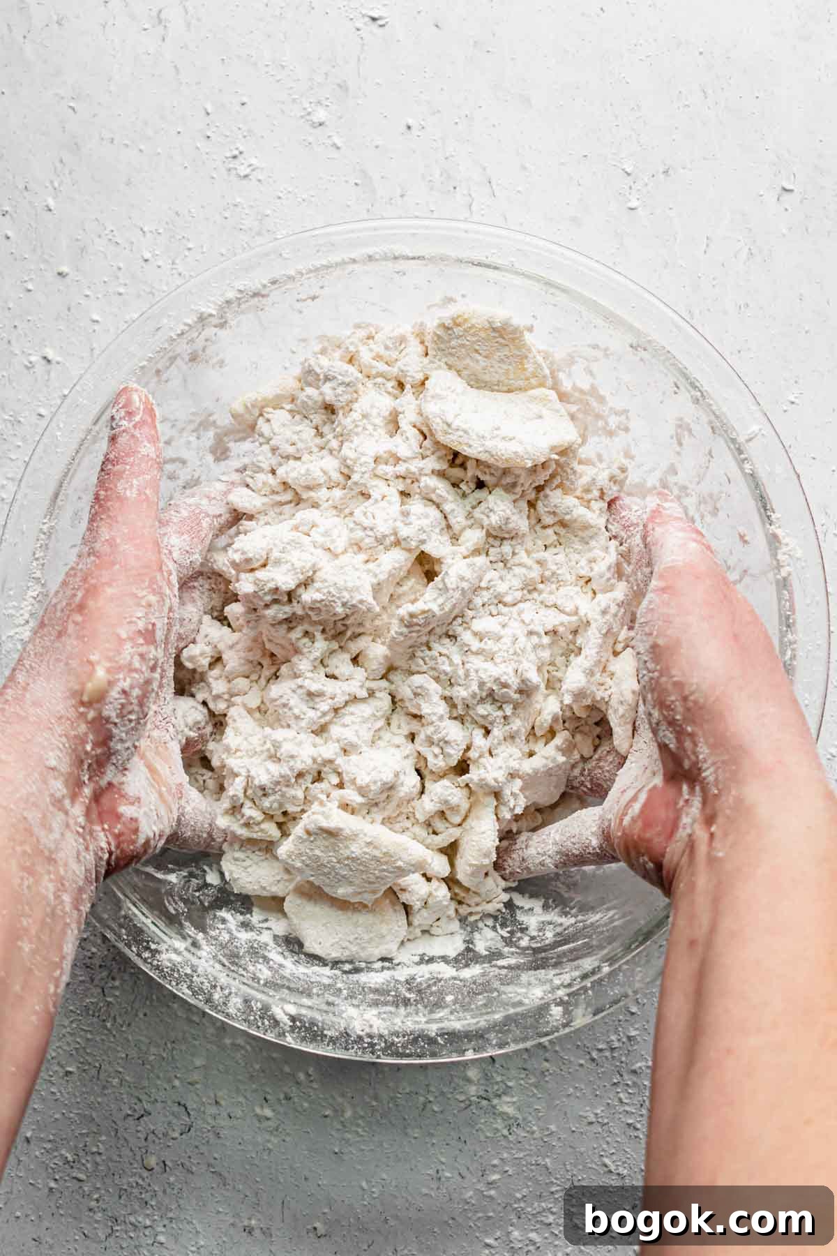 Two hands toss the butter, flour and water together.
