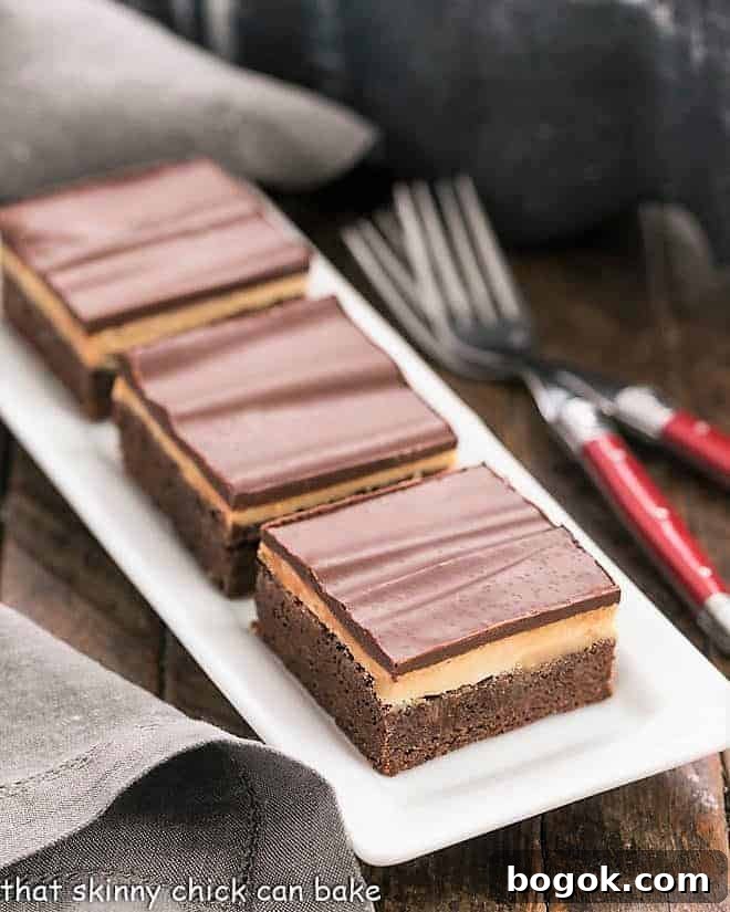 Peanut Butter Truffle Brownies - Fudgy brownies topped with a decadent peanut butter truffle filling and finished off with a dreamy chocolate ganache! 3 Peanut Butter Truffle Brownies on a white ceramic tray.