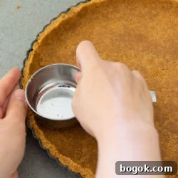 Graham Cracker Crust Being Pressed Into Tart Pan with Measuring Cup