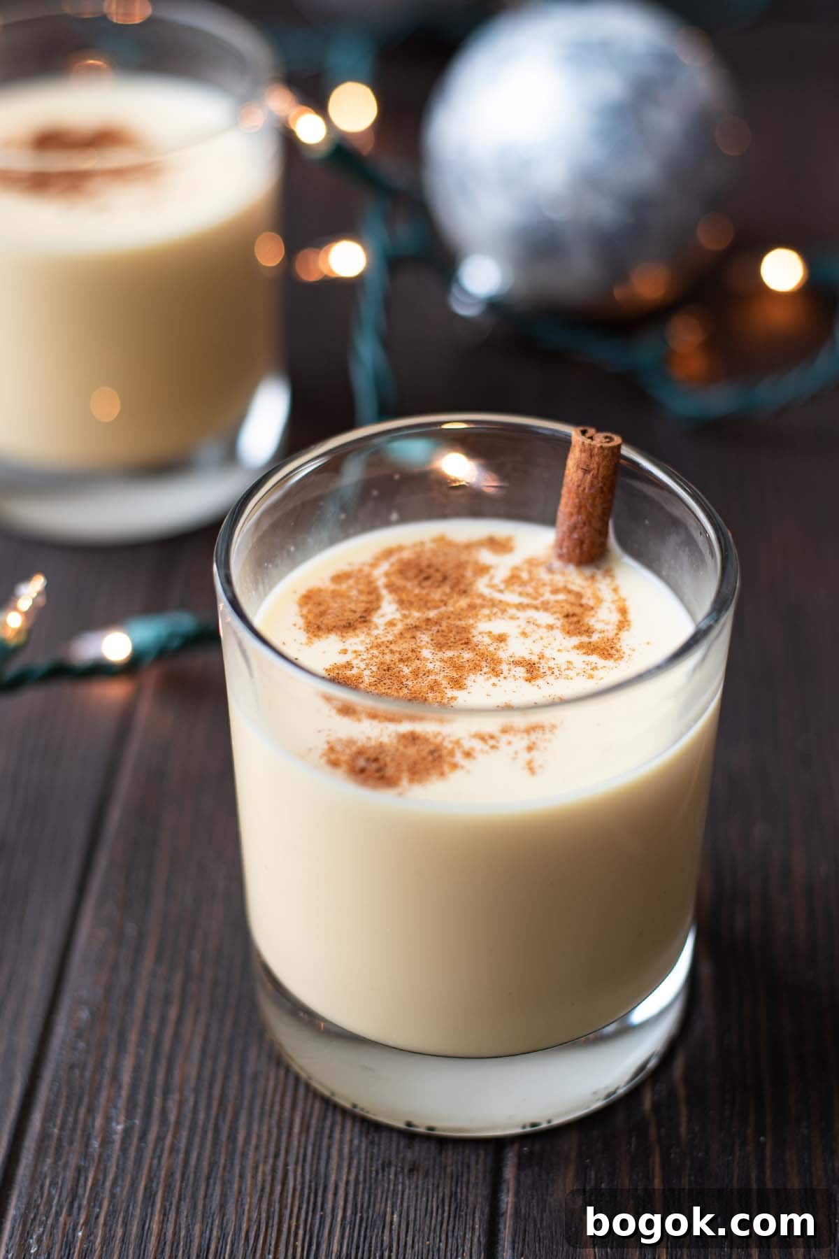 Creamy Eggnog Cocktail Recipe for Holiday Parties 2 An eggnog cocktail on a dark wooden table with Christmas ornaments and Christmas lights.