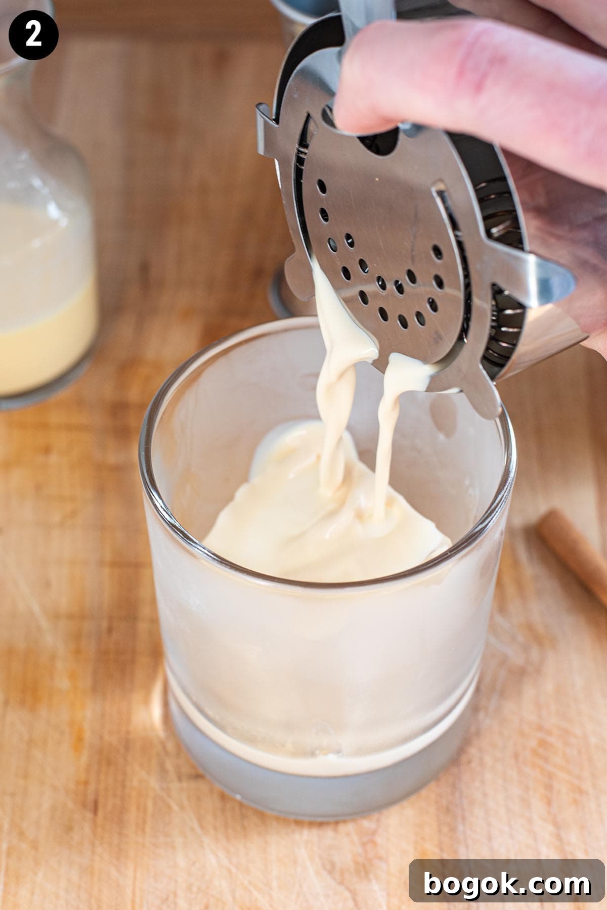 Creamy Eggnog Cocktail Recipe for Holiday Parties 5 Straining an eggnog cocktail into a chilled double old fashioned glass with a large ice cube.