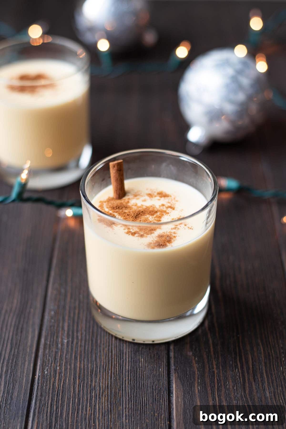 Creamy Eggnog Cocktail Recipe for Holiday Parties 7 An eggnog cocktail on a dark wooden table with Christmas ornaments and Christmas lights.