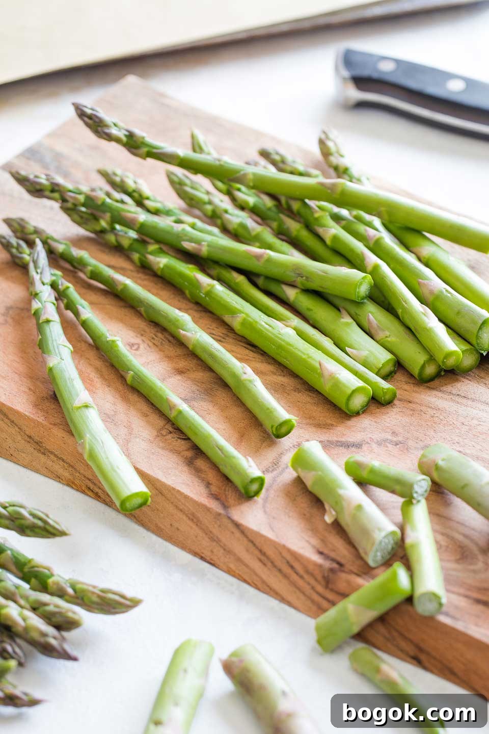 Asparagus spears on a cutting board, with the bottom inch or two of their stems just cut off.