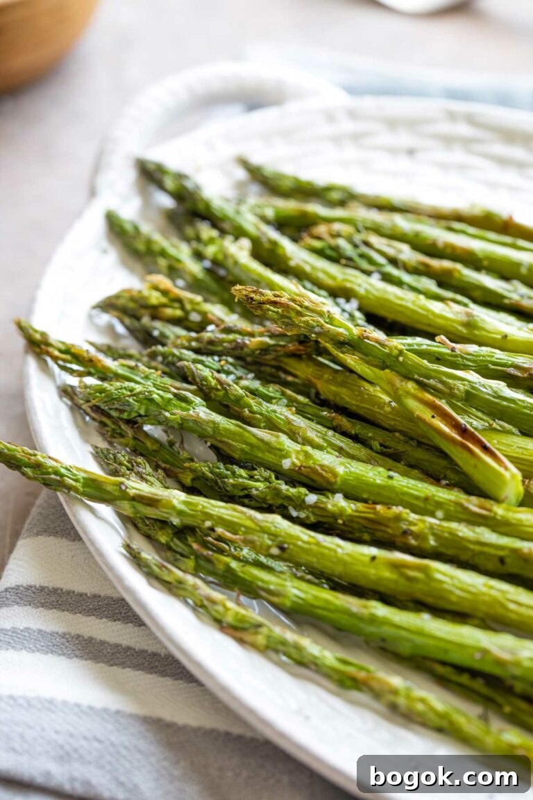 Finished asparagus heaped on white platter with fried spots and coarse salt