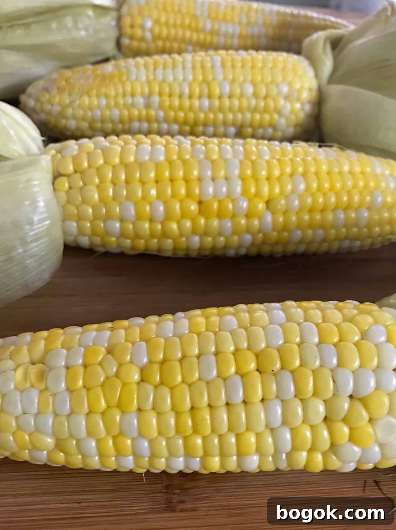 Smoked Corn on the Cob Recipe: Juicy Grilled Sweet Corn with Smoke 4 Corn on the cob with husks pulled back on wooden board close up side view