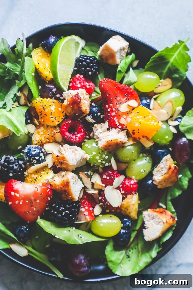 Picture of spinach salad with grapes, strawberries, blackberries, blueberries, raspberries, chicken, poppy seeds, hemp hearts, and a citrus poppyseed dressing on a black plate. 